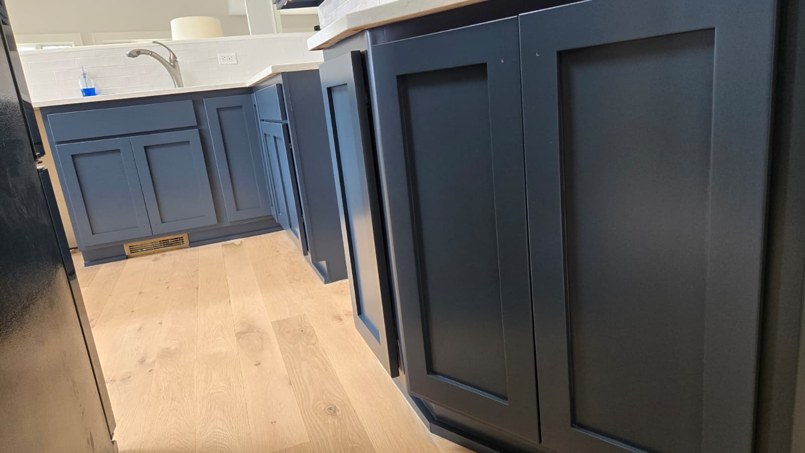 Gray-blue kitchen cabinets and island with white countertop and hardwood floors