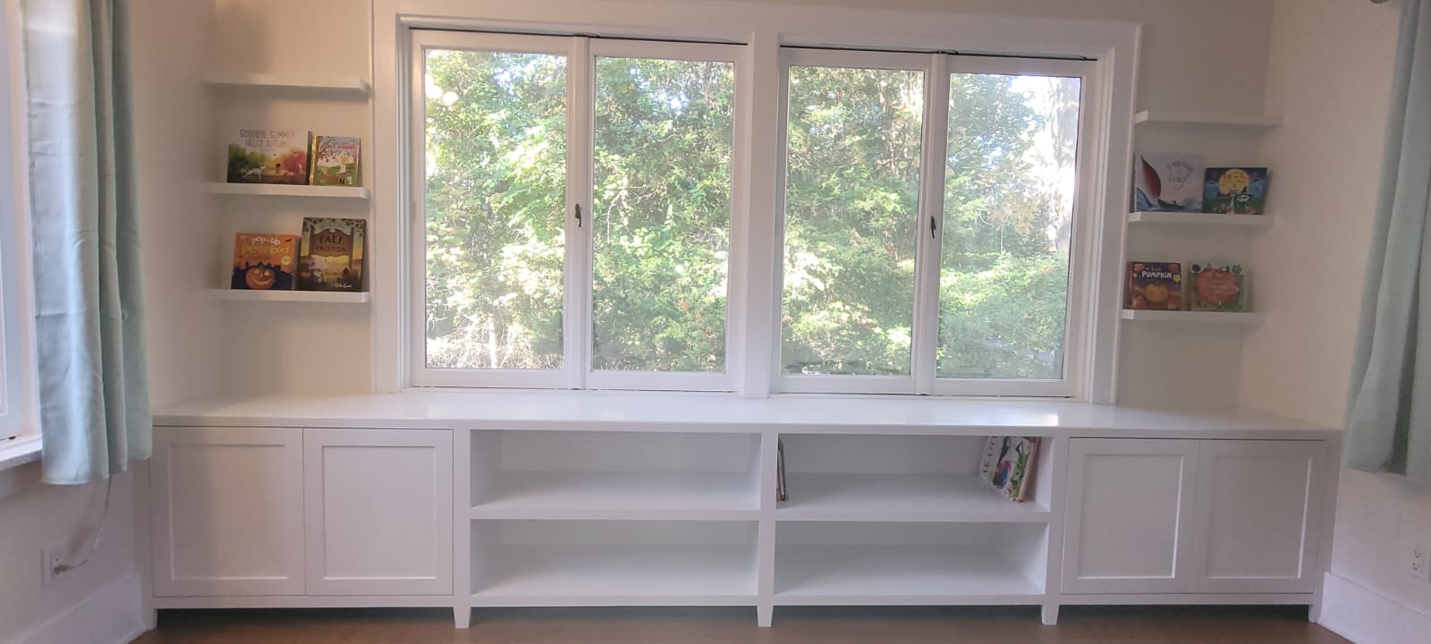 White custom built-in shelving and storage cabinets under windows